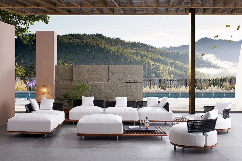 Outdoor living space with wooden modular seating design, white cushions, an ottoman, and a wooden low coffee table to match.